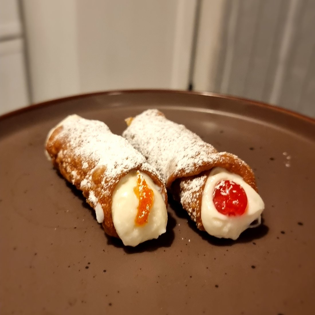 Due cannoli siciliani con ricotta e amarene su piatto scuro