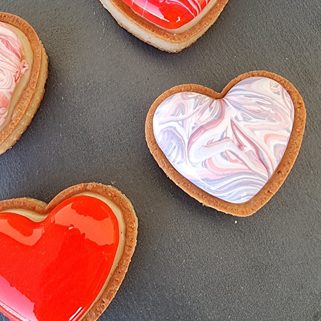 Tre cuori glassati con marezzature bianche su pietra scura